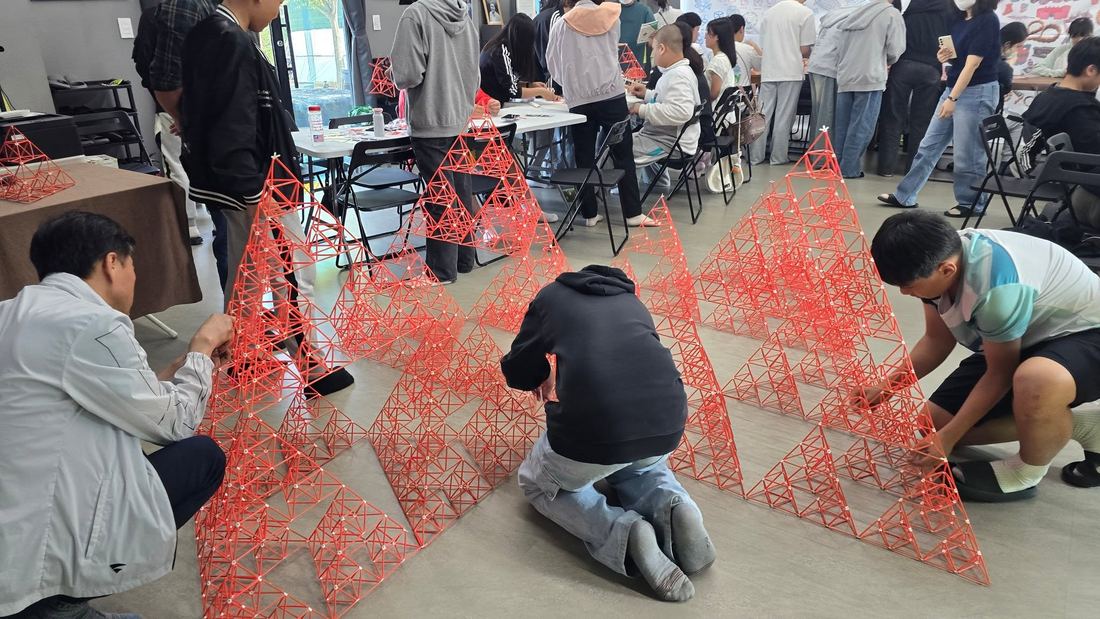 바닥에 펼쳐진 붉은 삼각형 구조물을 조립하는 학생들