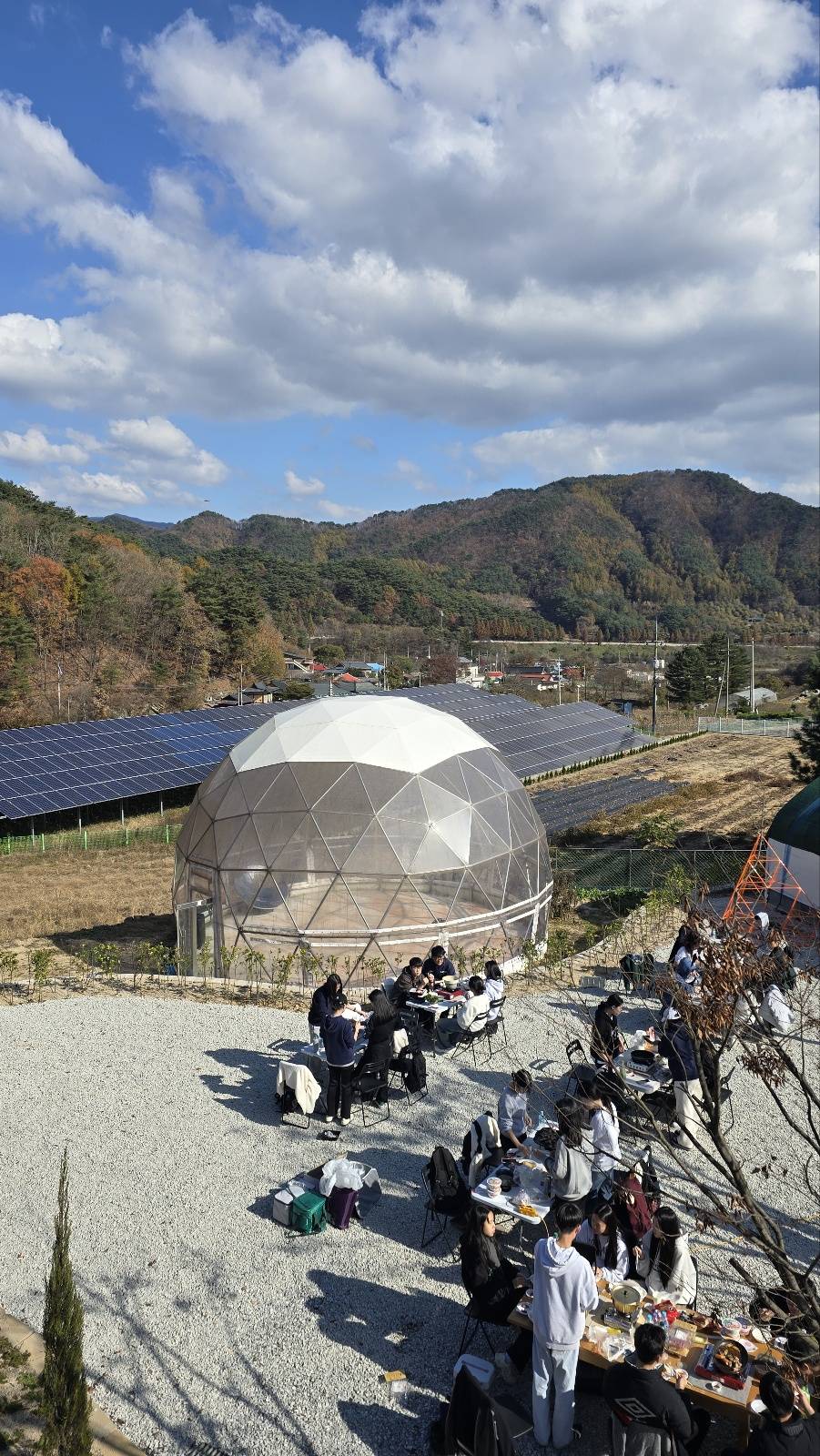 가을 산을 배경으로 한 지오데식 돔과 마당에 모인 학생들
