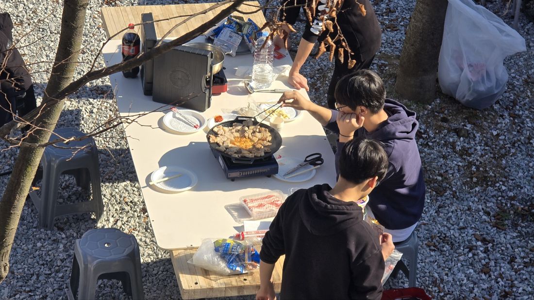 야외 테이블 위 화덕 주위에 모인 학생들
