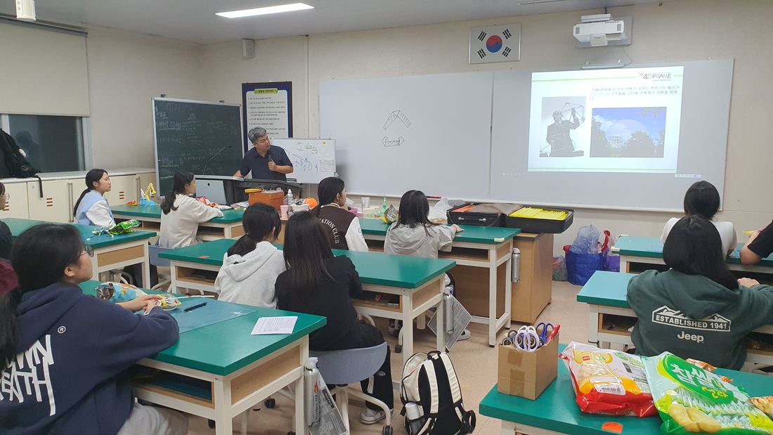 스크린이 켜진 교실에서 학생들이 책상에 앉아 수업을 듣고 있다