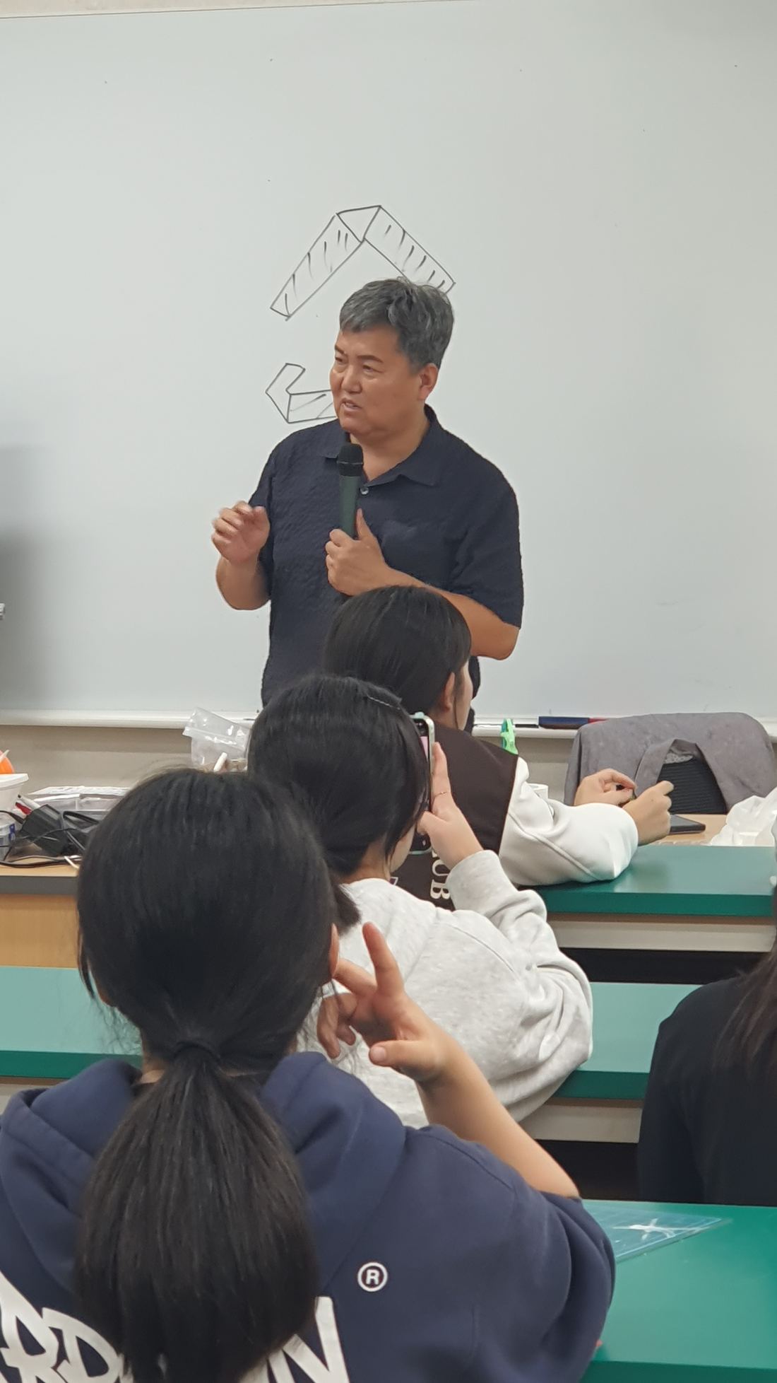 교실 앞에서 강사가 서서 설명하고 있고 학생들이 바라보고 있다