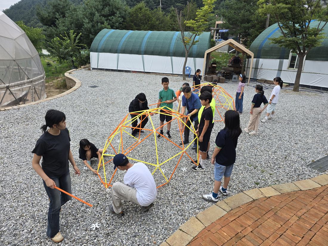 마당 바닥에서 아이들이 포디프레임 구조물을 조립하고 있다