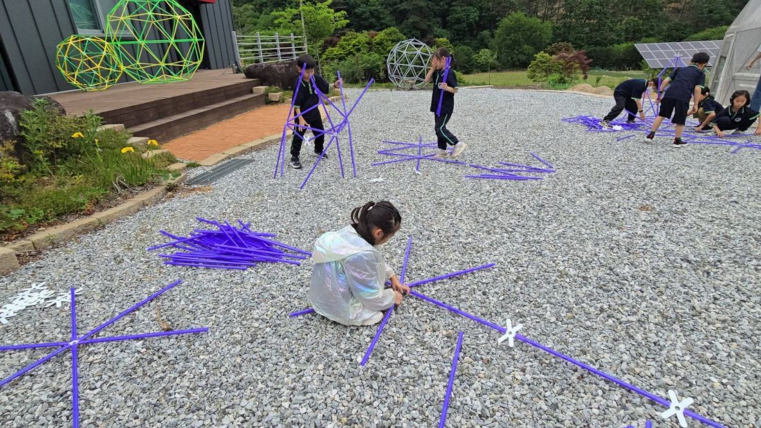 마당 자갈 위에서 보라색 구조물을 조립하는 아이들